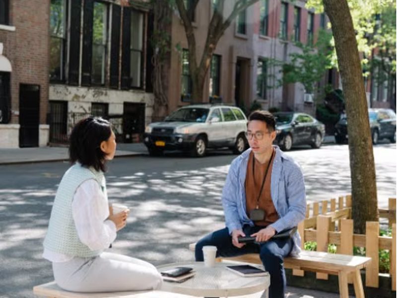 Two coworkers having a discussion on a sunny street bench